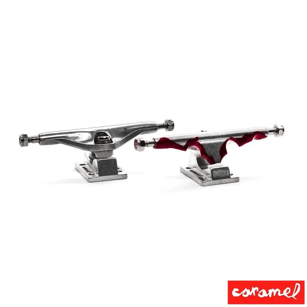 Two silver fingerboard trucks, one with a red, blood-splatter-like design, on a white background.
