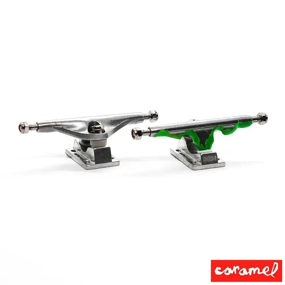 Two silver fingerboard trucks, one with green Halloween-themed accents, on a white background.